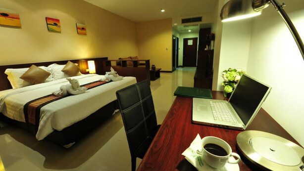 Quarto de hotel com cama, escrivaninha com laptop, xícara de café e um vaso de flores.