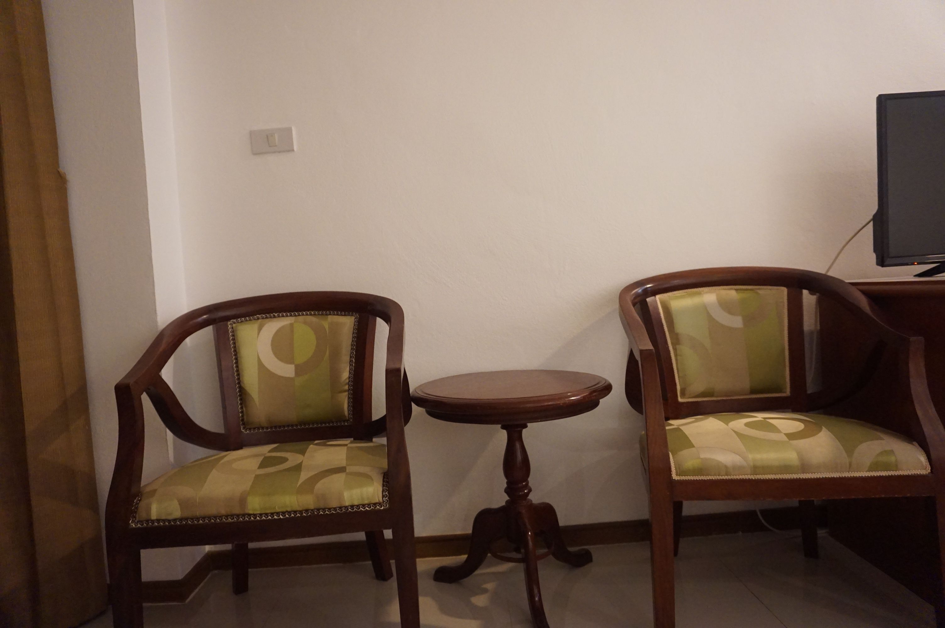 Two wooden chairs with cushioned seats and backs, a small round wooden table, and a television on a stand.