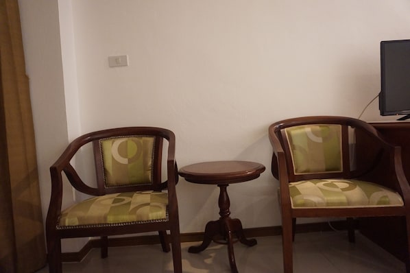 Dos sillas de madera con asientos y respaldos acolchados, una pequeña mesa redonda de madera y un televisor sobre un mueble bajo.