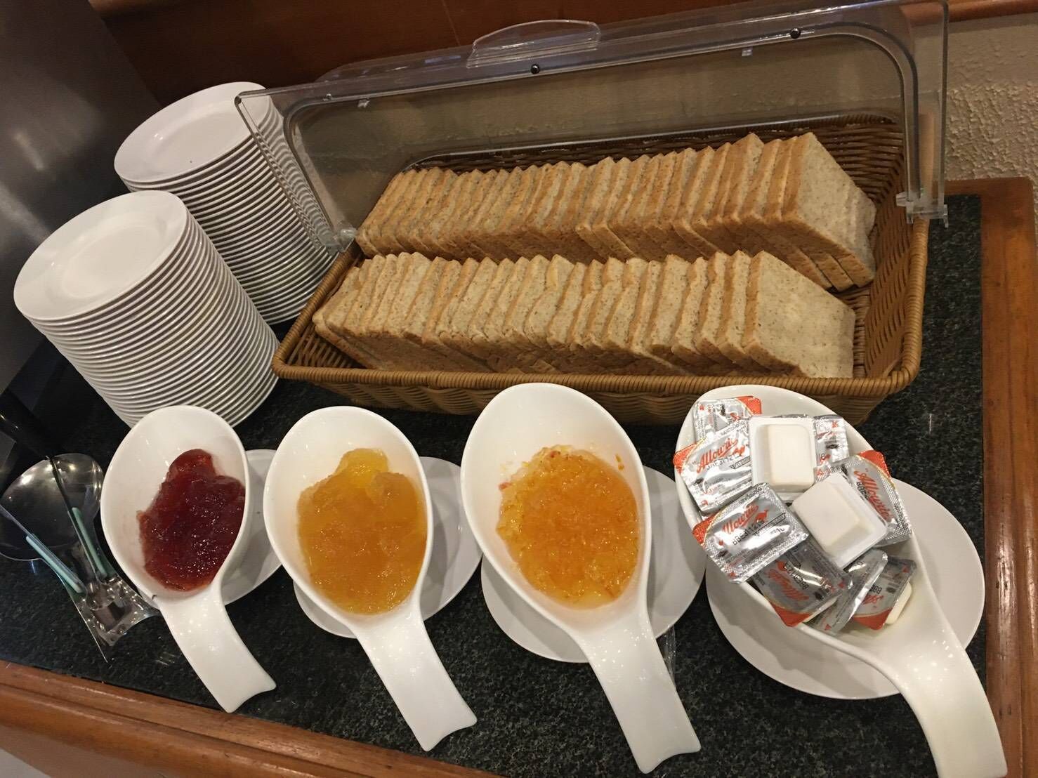 Montaje de bufé con pan en rodajas, recipientes de mermelada y paquetes de mantequilla.