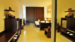 A hotel room with a bed, a desk, a chair, a TV, and a minibar. - Green World Palace Hotel (Songkhla)