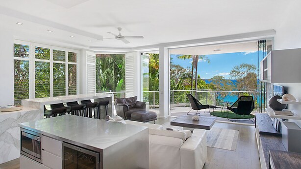 A modern kitchen with a large island, bar seating, and a view of the outdoors. - Allambi (Noosa Heads)