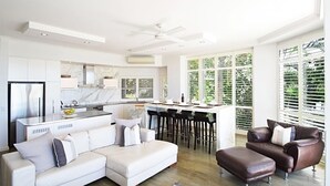 A modern kitchen with a white countertop, a built-in oven, and a dining area with a bar. - Allambi (Noosa Heads)