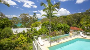 A pool with lounge chairs, surrounded by lush greenery and a clear blue sky. - Allambi (Noosa Heads)