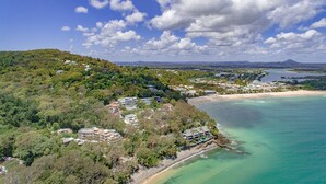 A coastal area with a beach, clear turquoise waters, and a hilly landscape with buildings. - Allambi (Noosa Heads)
