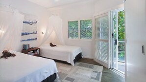 A bedroom with two beds, a ceiling fan, a window with blinds, and a view of greenery outside. - Allambi (Noosa Heads)