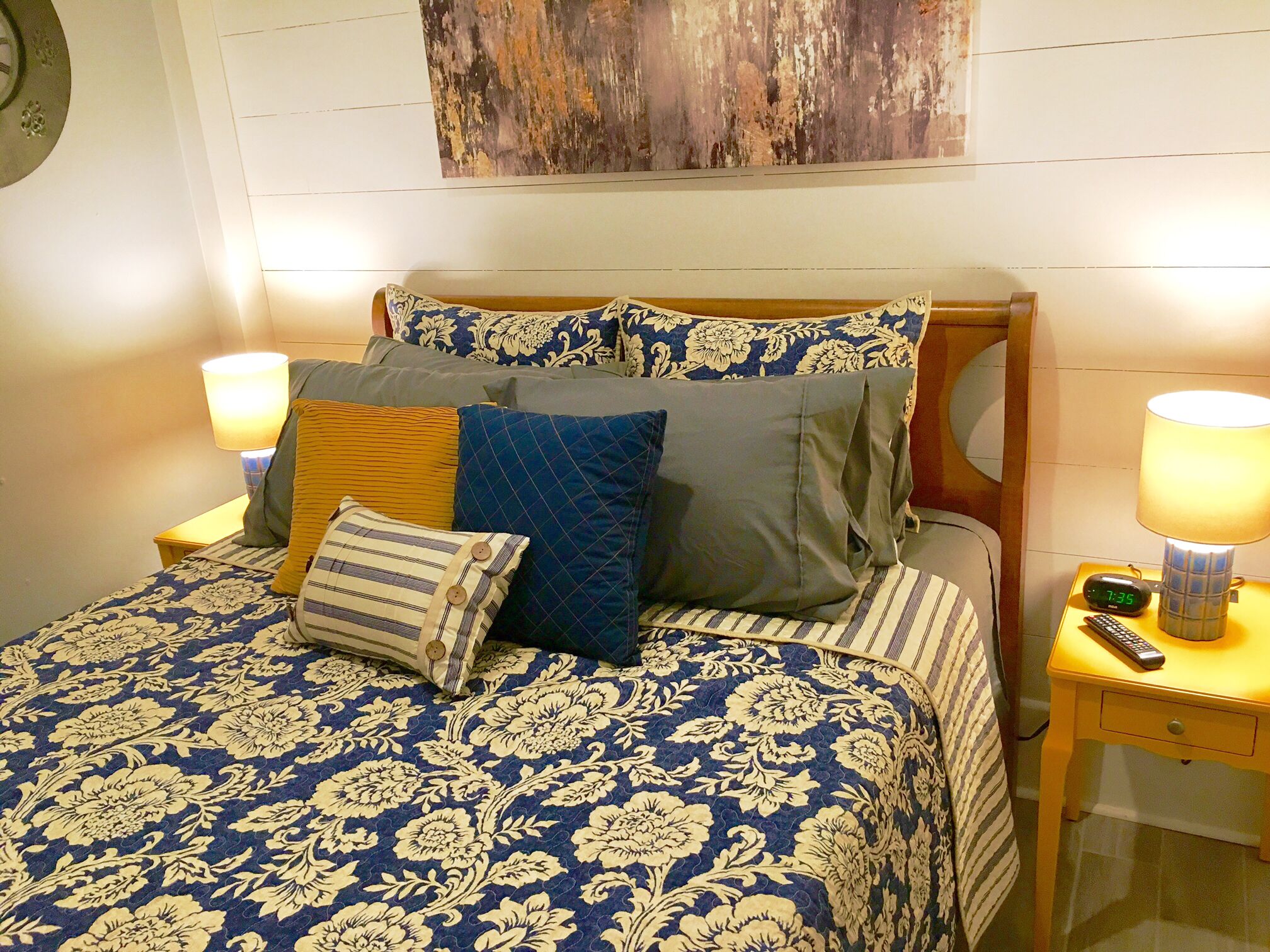 A bed with a floral-patterned bedspread, multiple pillows, two bedside lamps, and a wall clock.