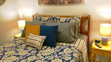 A bed with a floral-patterned bedspread, multiple pillows, two bedside lamps, and a wall clock.