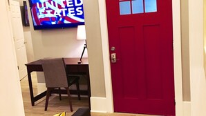 Una puerta roja con una ventana, un televisor mostrando 'United States', una mesa de comedor con sillas y una alfombra estampada.