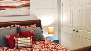 Un dormitorio con cama, almohadas, mesita de noche, lámpara y una puerta.