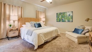 Quarto com cama, mesa de cabeceira, abajur, ventoinha no teto e um quadro na parede.