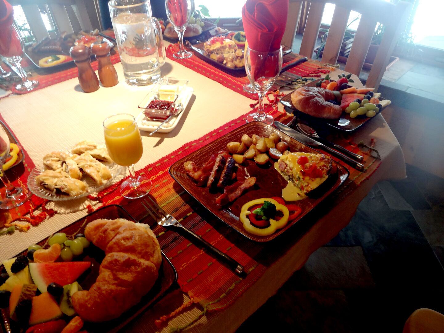 A breakfast buffet with various dishes, including pastries, fruits, and a hot plate with eggs and bacon.