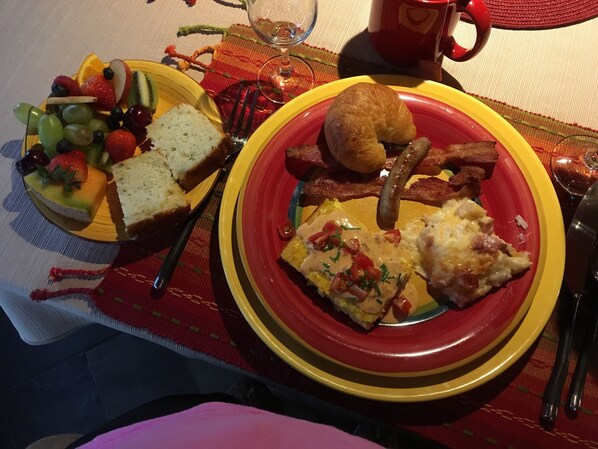 A breakfast setting with a plate of eggs, sausage, and toast, and a bowl of fruit and bread. - FOREST GARDENS GETAWAY B&B (Watersmeet)