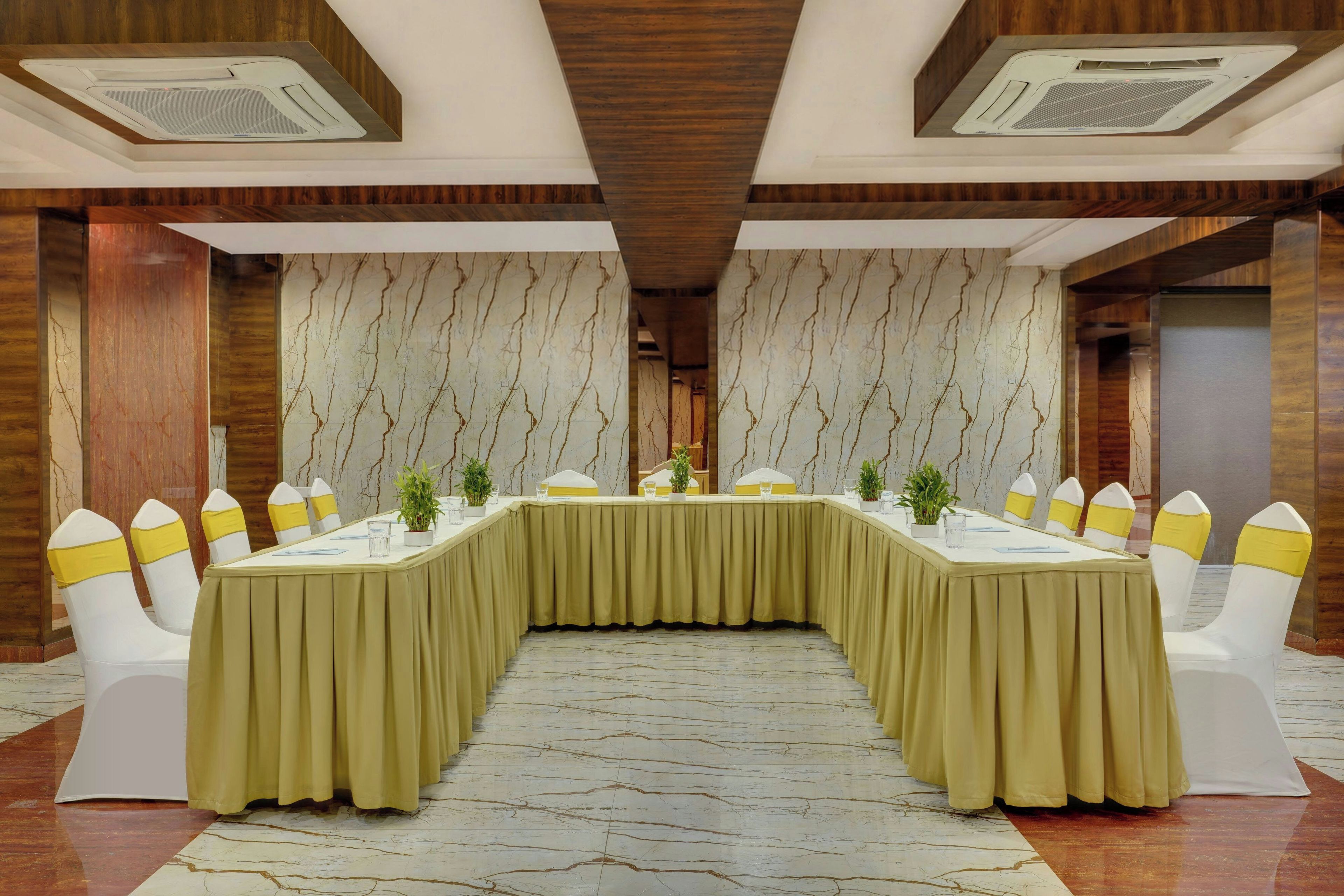 A conference room with a long table, white chairs with yellow sashes, and marble-patterned walls.