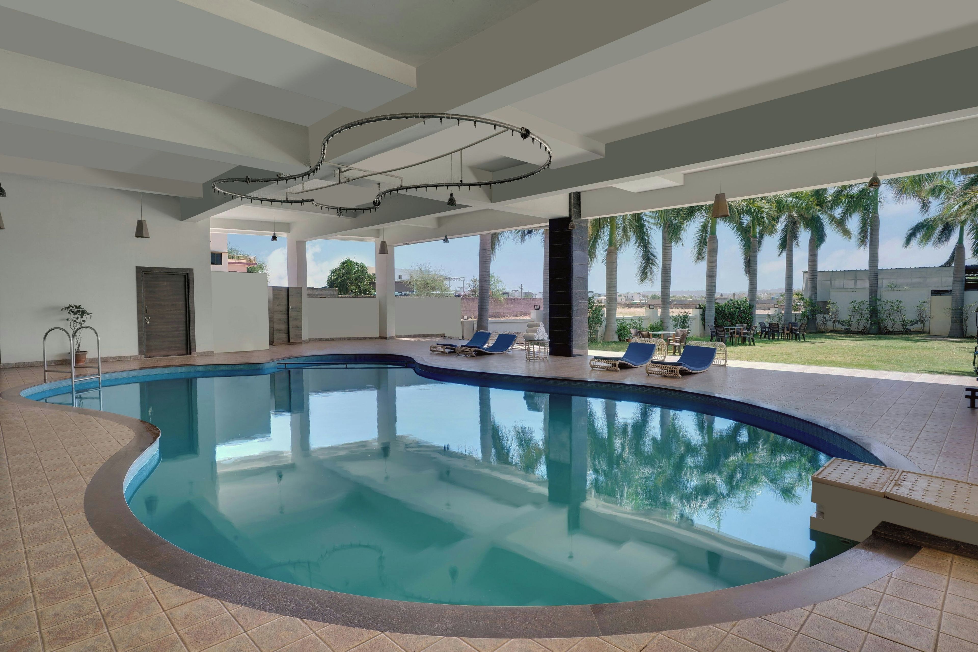 A swimming pool with a curved edge, surrounded by lounge chairs and a patio area with a view of palm trees and buildings.