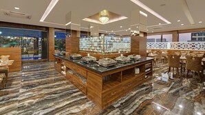 A modern hotel lobby with a marble floor, a central buffet area, and a seating area with tables and chairs.