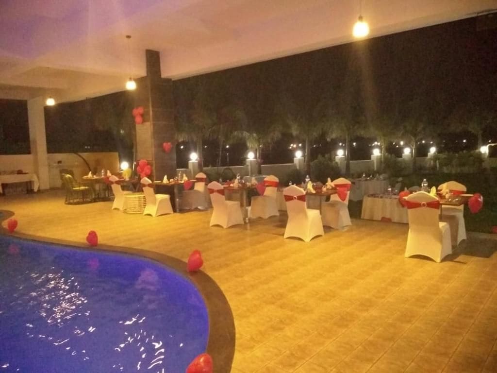 An indoor pool area with tables and chairs arranged for dining or socializing, surrounded by a tiled floor and a pool with water.