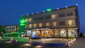 A modern hotel with a prominent green sign, a well-lit entrance, and a landscaped outdoor area with a fountain.
