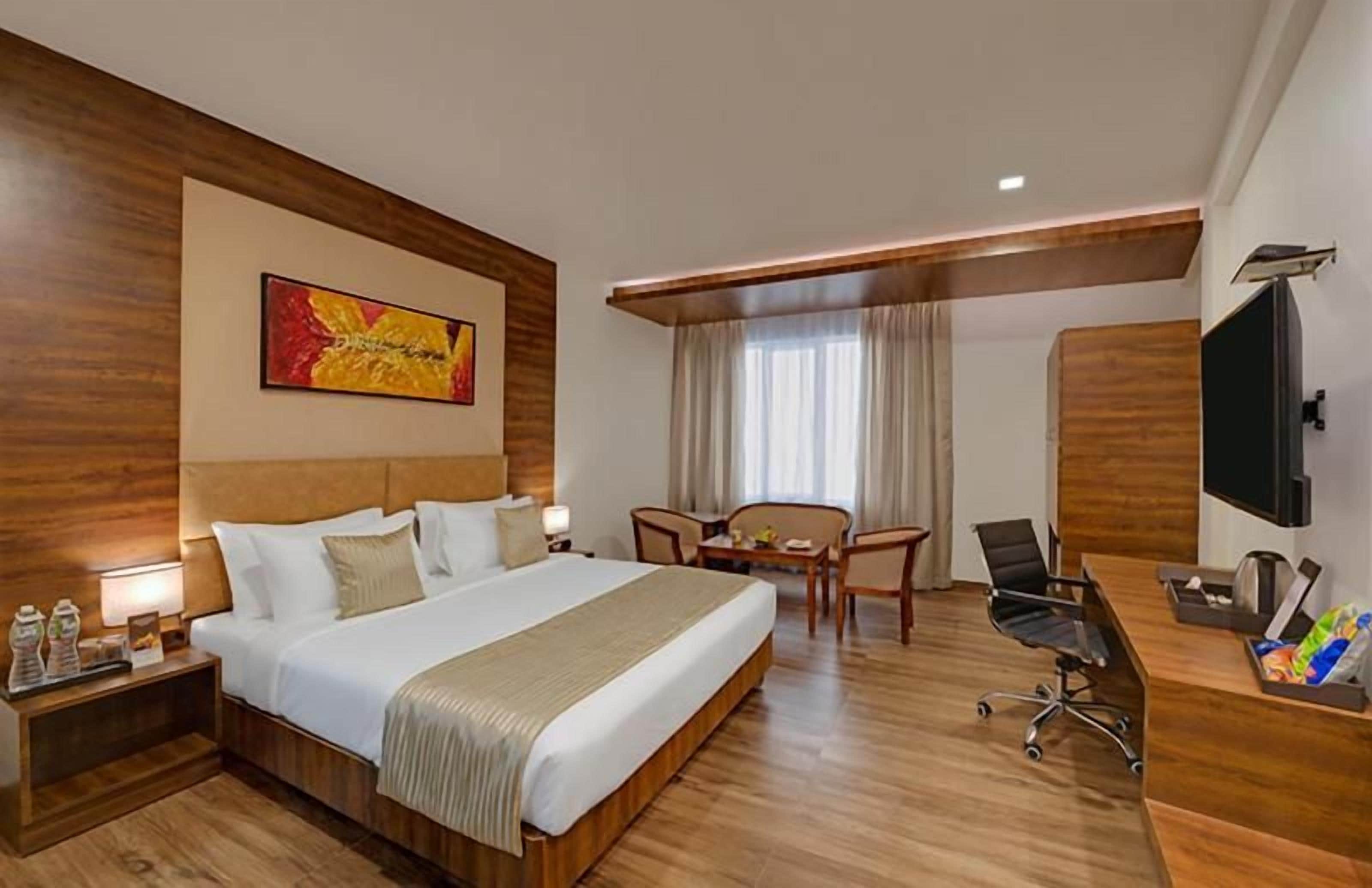 Habitación de hotel con una cama grande, un escritorio, una silla, un televisor y un cuadro en la pared.