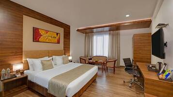 Habitación de hotel con una cama grande, un escritorio, una silla, un televisor y un cuadro en la pared.