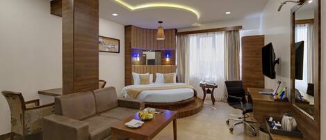 A hotel room with a bed, a sofa, a desk, a chair, a TV, and a bathroom with a shower and toilet.
