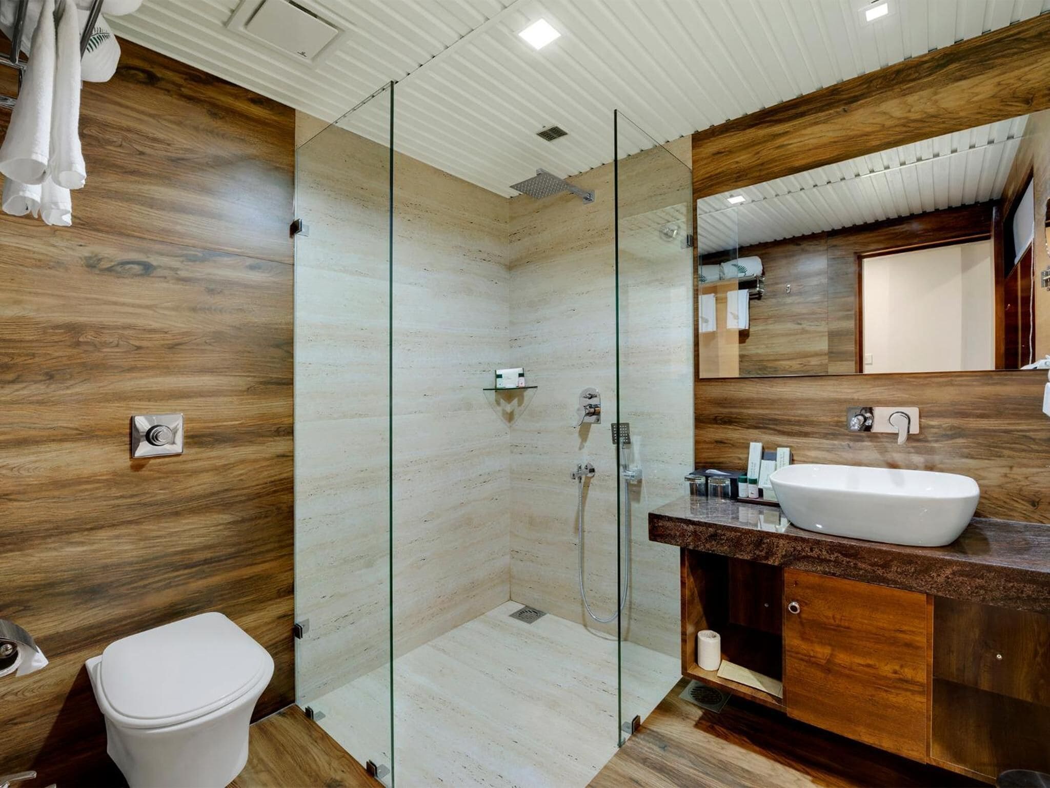Un baño moderno con ducha de vidrio, tocador de madera con lavamanos y un inodoro.