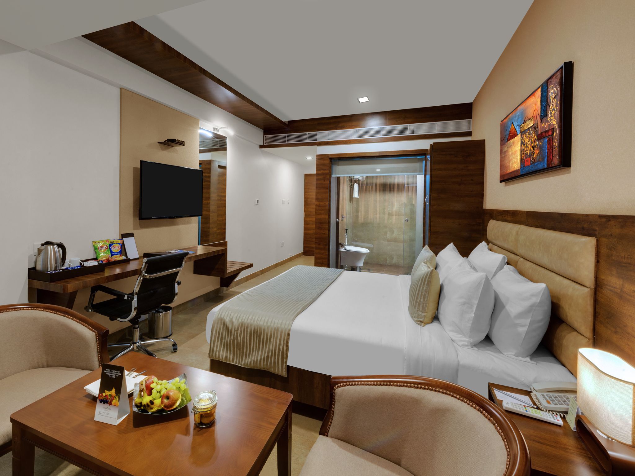 A hotel room with a bed, desk, chair, and a TV.