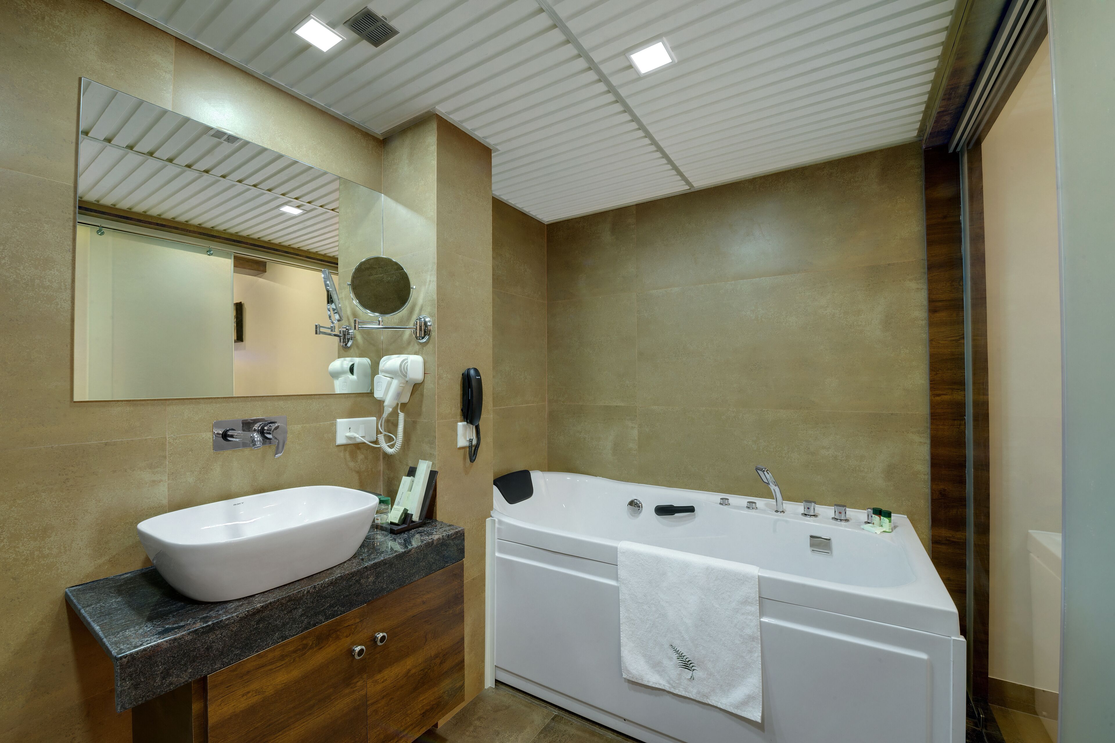 A modern bathroom with a large white bathtub, a sink with a marble countertop, a mirror, and a hairdryer.