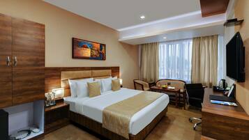 A hotel room with a large bed, a desk, a chair, a television, and a painting on the wall.