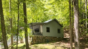 A wooden deck leading to a cabin with a stone foundation, surrounded by a forest.