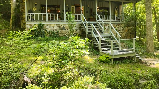 A cabin with a stone exterior, wooden deck, and a staircase leading to the entrance.