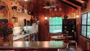 A wooden interior with a bar area, wicker chairs, a refrigerator, and a window with a view of greenery.