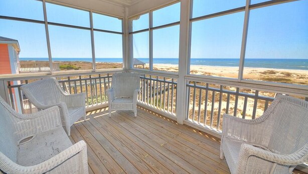 A covered porch with wicker chairs and a view of the beach.