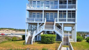 A two-story beachfront house with a balcony on each floor, a covered porch, and a staircase leading to the upper level.