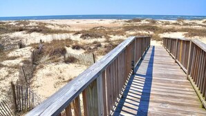 A wooden boardwalk leading to a beach with dunes and a clear sky.