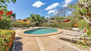 Ein kreisförmiger Pool mit Liegestühlen, umgeben von tropischer Vegetation und Palmen.