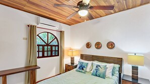 Ein Schlafzimmer mit Bett, Deckenventilator, Fenster mit Vorhängen und Wanddekoration.