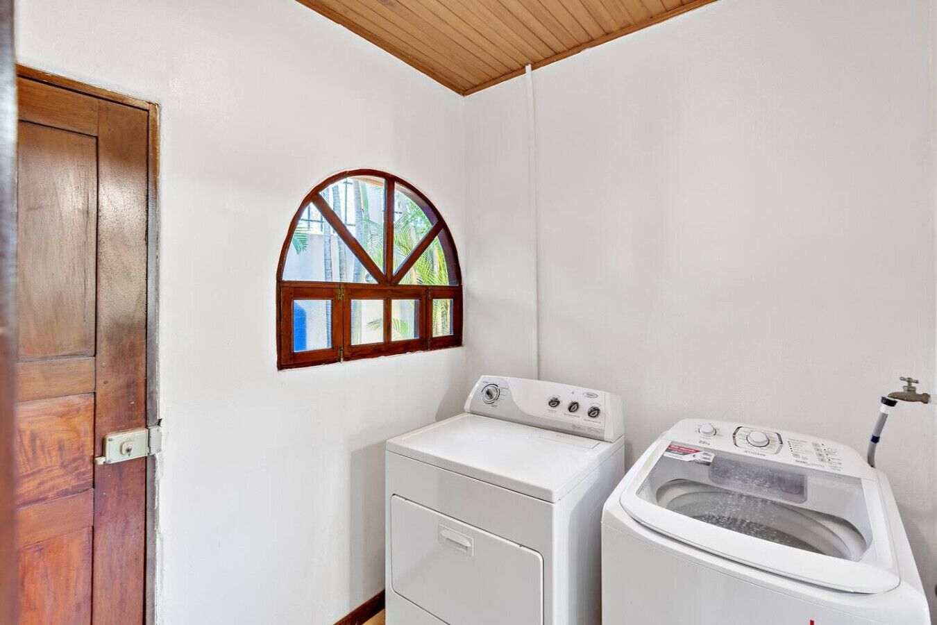A laundry room with a wooden door, a window with a wooden frame, and two white washing machines.