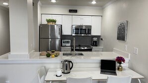 A modern kitchen with white cabinetry, stainless steel appliances, and a small dining area with white chairs and a laptop.