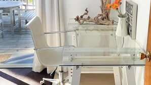 A modern room with a glass desk, white chair, decorative items, and a view of the outdoors.