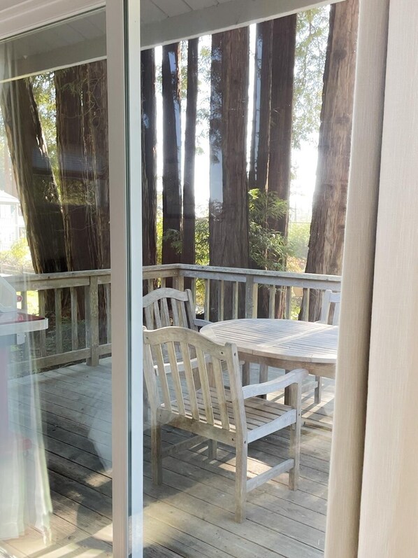 A wooden deck with a table and chairs, overlooking tall trees.