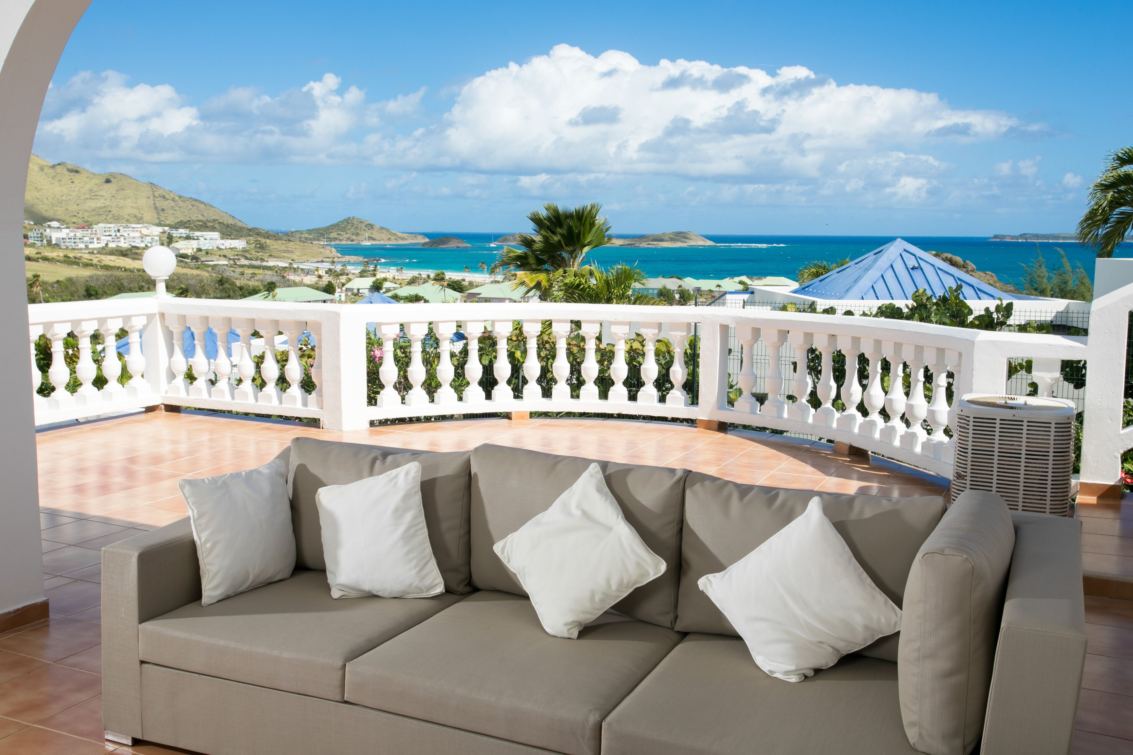 Un balcon avec un canapé beige, des coussins blancs et une balustrade blanche.