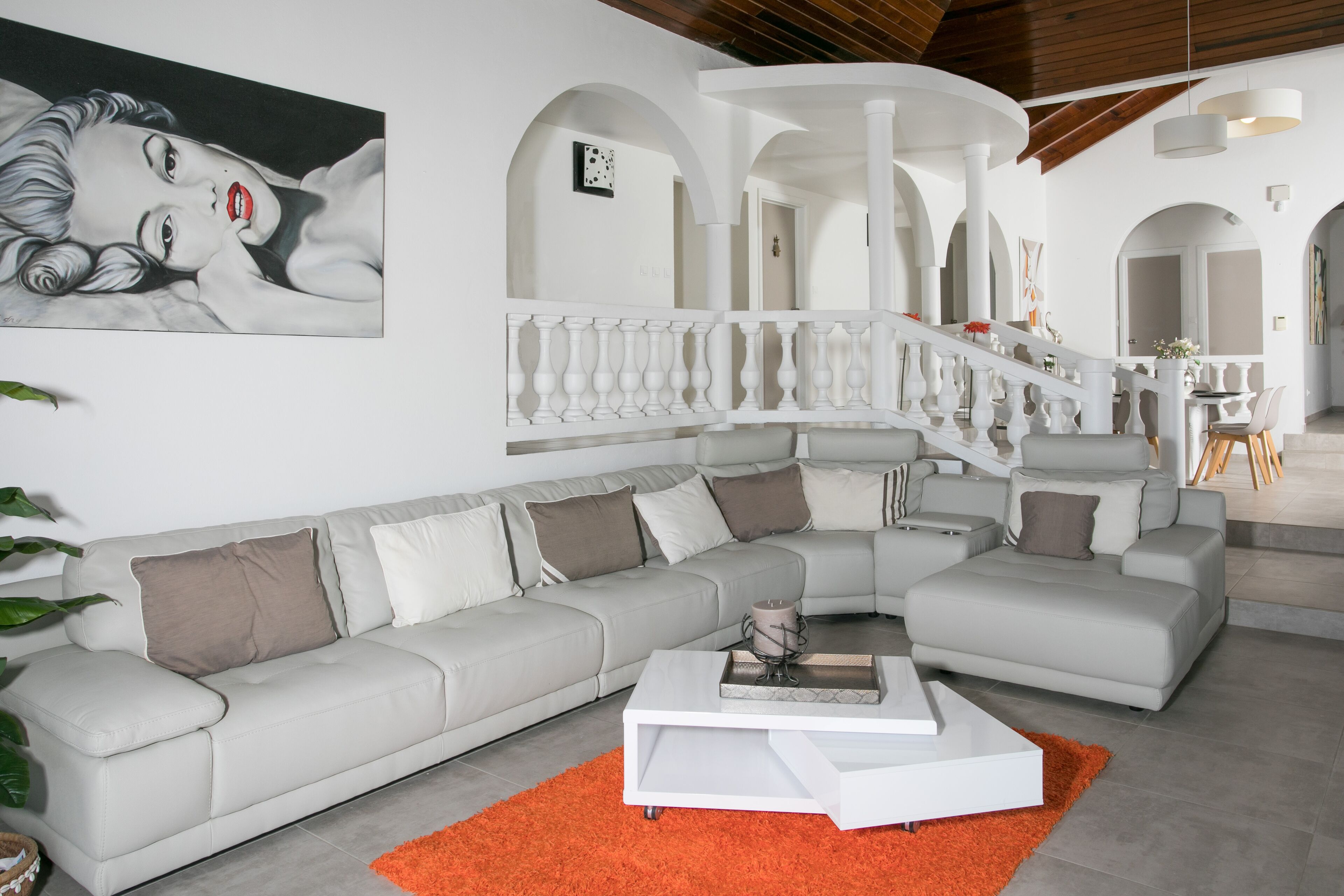 Un salon moderne avec un grand canapé d’angle, une table basse blanche et un escalier doté d’une balustrade blanche.