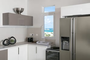 A modern kitchen with a built-in water dispenser, a stainless steel refrigerator, and a window with a view of the ocean.