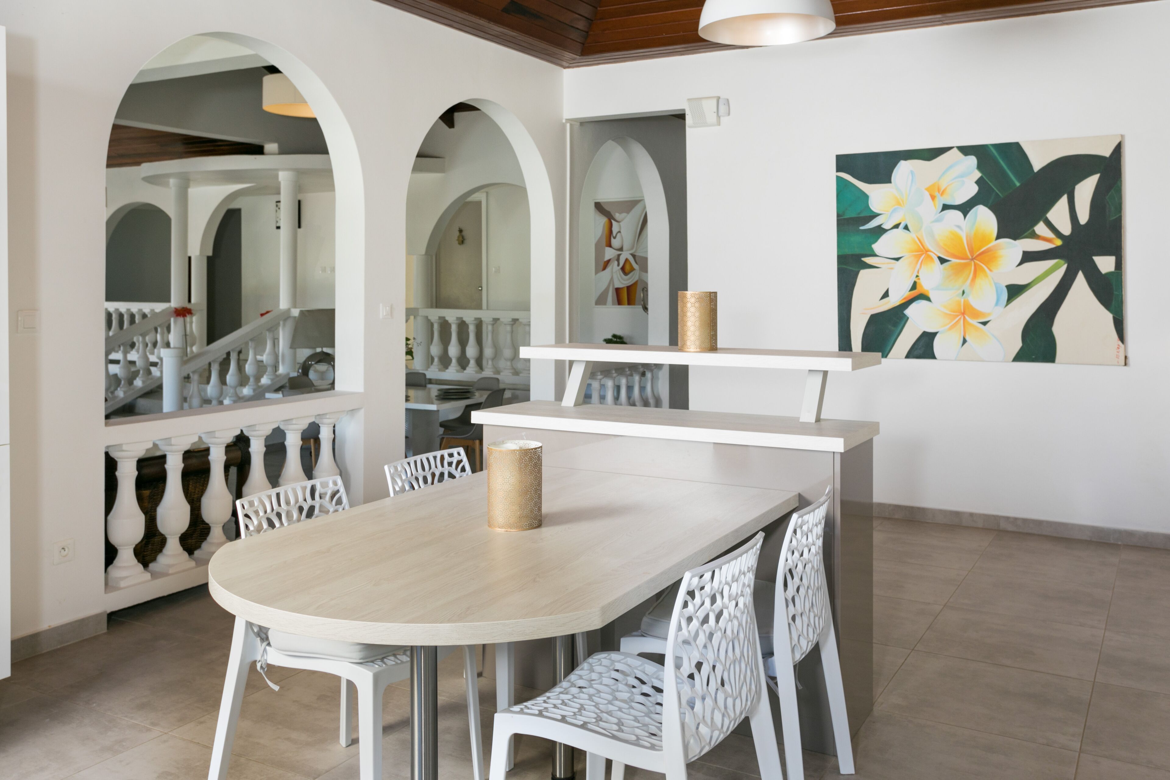 A dining area with a round table, white chairs, and a painting of flowers on the wall.