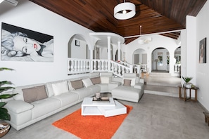 A spacious living room with a white sectional sofa, a white coffee table, and an orange rug. There is a staircase with a white railing leading to another level.
