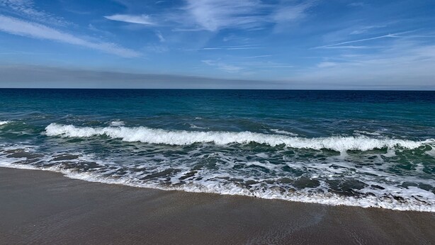 Een strand met golven die op het strand breken onder een heldere lucht.