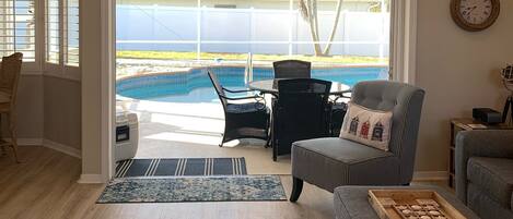 A living room with a view of a swimming pool, a ceiling fan, and a sign above the door.