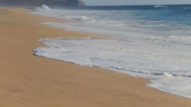 Una playa con arena dorada y olas rompiendo sobre ella.
