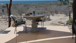 Un patio al aire libre con una mesa, sillas, un toldo amarillo y vista al océano.
